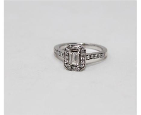 A platinum and diamond cluster ring, the central emerald cut stone weighing approximately 0.4 carat, size J