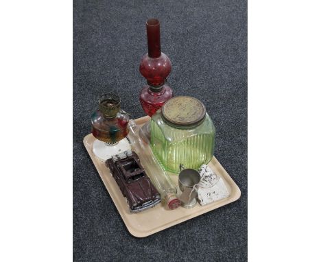 A tray of two early 20th century oil lamps, vintage green glass storage jar with lid, glass rolling pin, cast iron lion mask 