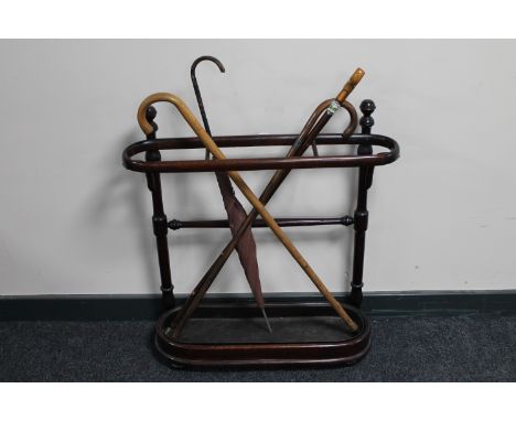 An antique Bentwood stick stand with metal tray containing three vintage walking sticks and a parasol 