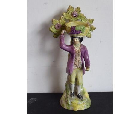 An early 19th century ceramic Bocage; gentleman in 18th century dress carrying a grape hod basket upon his head (18.5cm high)