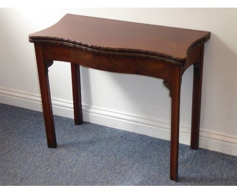 A mid-18th century serpentine-fronted mahogany fold-over top card table; green-baize interior above the edges carved with flo