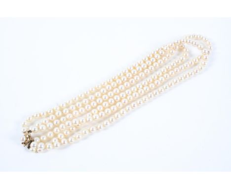 A three row cultured pearl necklace. 6 to 6.50mm pearls strung plain and finished with a yellow metal floral clasp set with a