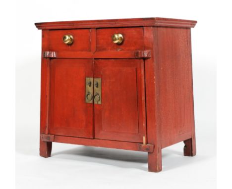 An Chinese red painted hardwood cabinet, with two drawers above two cupboard doors, applied with scroll ornament, on stile fe