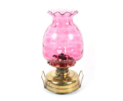 A large cranberry glass and brass oil lamp, early 20th century, the later frilled-rimmed shade mould blown with dimples, on d