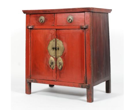 A Chinese red painted hardwood cabinet, with two drawers above two cupboard doors enclosing a shelf, applied with scroll orna