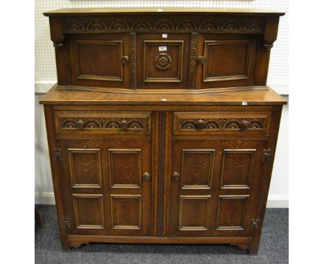 An early-20th Century oak sideboard, oversailing top, heavily carved to frieze, central carved stylised English rose panel, f