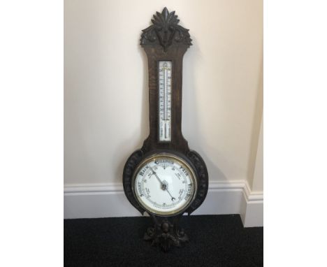 A late 19th/early 20th Century aneroid banjo barometer, with upper glazed thermometer and carved decoration.