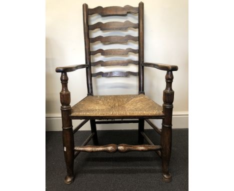 A 19th Century style oak framed rush seated ladder-back elbow chair, raised on turned front supports united by stretchers.