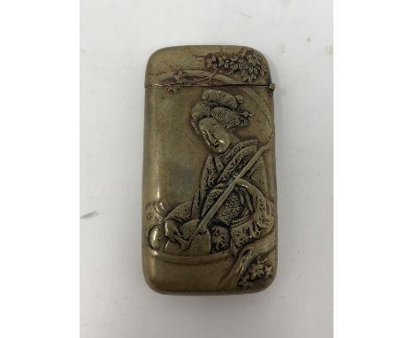 A Japanese brass vesta/card case decorated with a figure of a Geisha lady playing an instrument.