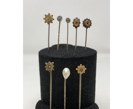 An assortment of eight mostly yellow precious metal tie pins set with turquoise, pearl, ruby etc.