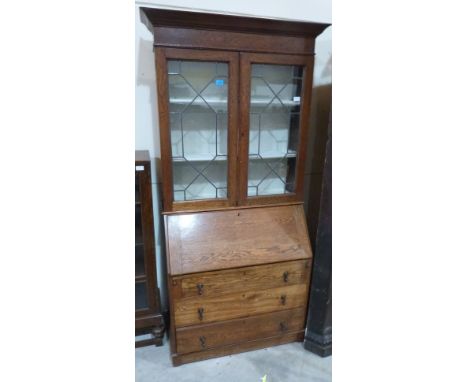 A 1930s oak bureau bookcase, enclosed by a pair of leaded light doors over sloping fall and three long drawers. 34' wide