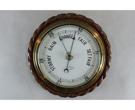 A circular barometer with white dial and scale 26 to 31 inches, with market and pointer, in carved oak case, 23cm diameter