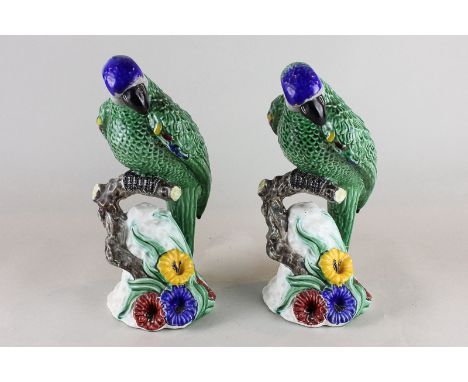 A pair of ceramic models of parrots, green glaze with blue crowns, perched on floral rocky base, 28cm