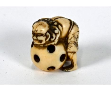 A 19th century Japanese carved ivory netsuke of a primitive figure leaning over a pierced ball with a small internal loose ba