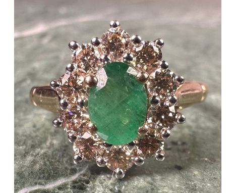 An emerald and diamond cluster ring, central oval mixed cut emerald approx 0.85ct, surrounded by ten round brilliant cut diam