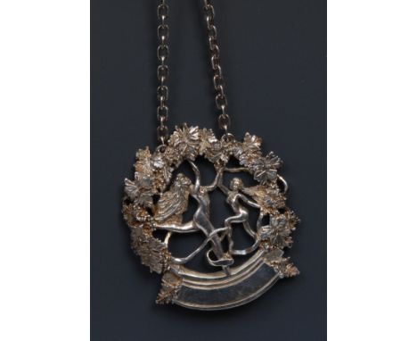 An Elizabeth II silver wine label, cast with nude maenads dancing beneath fruiting vine, 5cm wide, LWJ, London 1982 