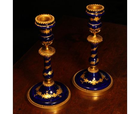 A pair of 19th century French gilt metal mounted enamel table candlesticks, decorated with bands of fruiting vine on a Bleu R