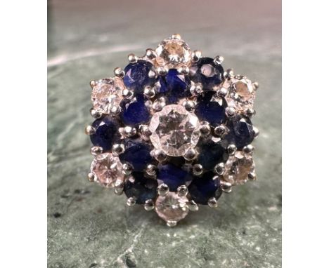 An 18ct gold diamond and sapphire flowerhead cluster ring, the central brilliant cut diamond flanked by six smaller, accented