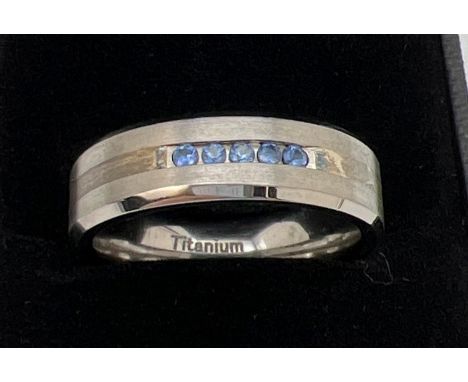 A brand new in box man's Titanium and Sapphire band ring. Two tone titanium with 5 round cut channel set blue sapphires. With