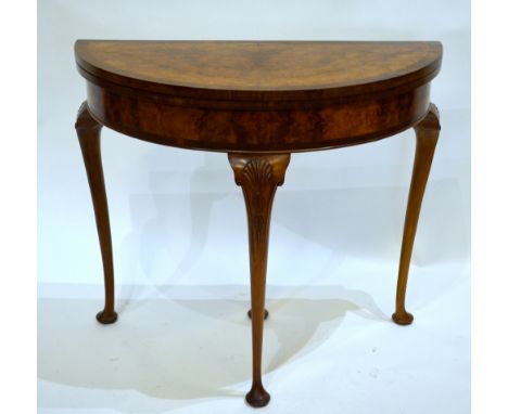 A Georgian style cross-banded burr walnut demi-lune card table, raised on hip shell carved cabriole legs