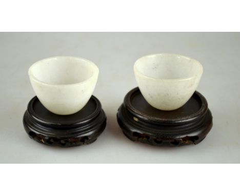 A pair of Chinese mutton-fat jade small bowls, probably 19th century, each 5 cm dia c/w associated wood stands (2)