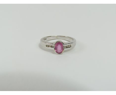 A white gold pink sapphire and diamond dress ring, the oval facetted sapphire three quarter rub over set with three round bri