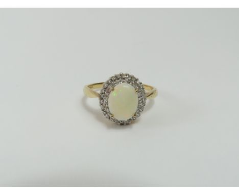 A 9ct gold white opal and diamond cluster ring, the oval cabochon cut opal surrounded by two rows of round diamonds, finger s