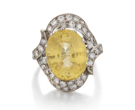 A YELLOW SAPPHIRE AND DIAMOND CLUSTER RING an oval-cut yellow sapphire within a scrolling milgrain border of round brilliant-