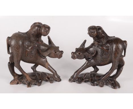 A pair of Chinese hardwood figures of buffalos, each with a male rider, early 20th century, with silver wire inlay, height 21