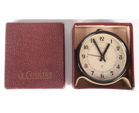 A Le Coultre alarm clock, circa 1930s, in a black circular case on a cream shaped stand, in original box, height 8cm, width 7