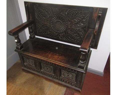 A carved oak monks bench, circa 1920s, the seat with a hinged lid above a triple panelled front and plinth base, height 116cm