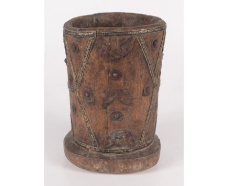 An African wooden mortar, with applied metal abstract decoration, height 29cm, diameter 20cm. 