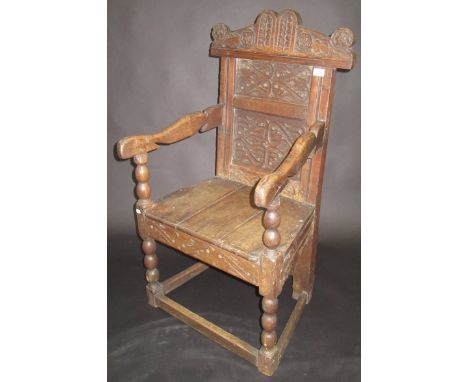A 17th century carved oak joined chair with open arms, bobbin turned supports, shaped crest rail and two panels to the back, 