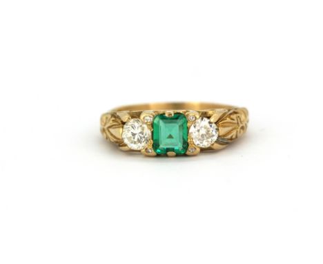 A yellow metal (tested 18ct gold) ring set with an emerald cut natural emerald flanked by brilliant and old cut diamonds, (M.