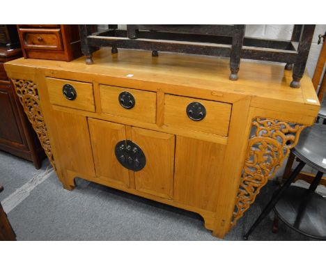 A Chinese light elm sideboard with three drawers and a pair of doors, flanked by carved and pierced bracket supports.