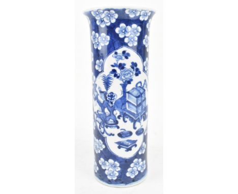 A Qing dynasty blue and white sleeve vase. The flared rim vase decorated with two open panels depicts tables, vases, boxes, f