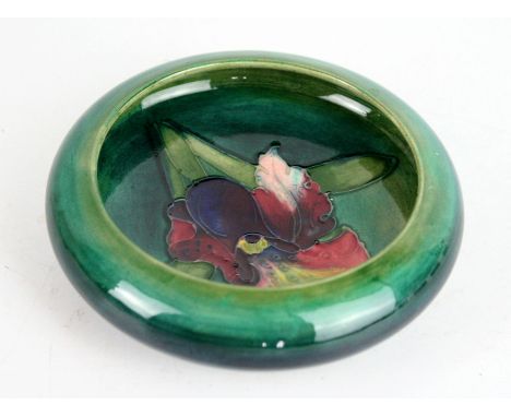 A Walter Moorcroft pottery dished bowlDecorated in the Orchid pattern on a green ground, impressed factory marks to base, dia