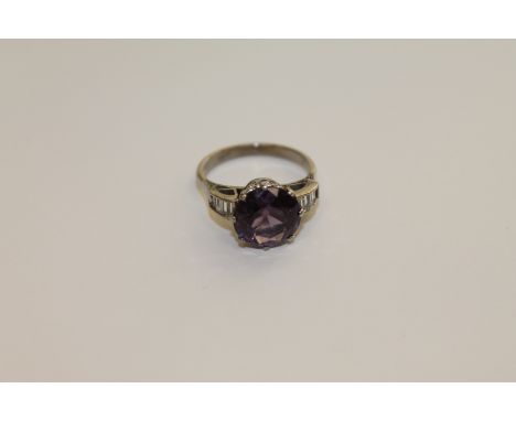 An 18ct white gold Alexandrite ring, a brilliant cut Alexandrite within a claw setting, to baguette cut diamond set shoulders