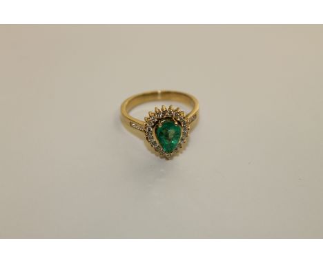 An 18ct gold emerald and diamond ring, a pear cut emerald within a border of brilliant cut diamonds, to diamond set shoulders