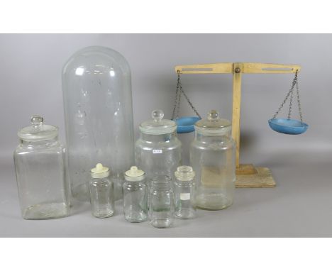 Seven clear glass storage jars, a Victorian glass dome and a pair of childrens wooden weighing scales.