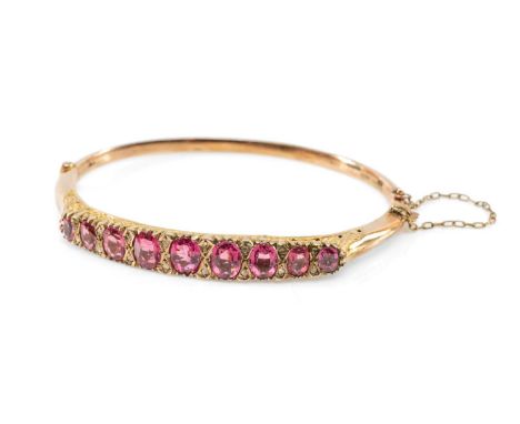 YELLOW METAL PASTE & DIAMOND CHIP HINGED BANGLE, having nine graduated oval pink paste stones, safety chain, 7.6gmsProvenance