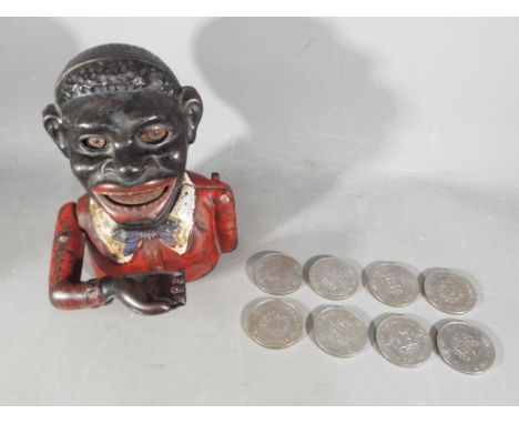 A vintage cast iron mechanical money bank in the style of a black man, approximately 16 cm (h) and eight commemorative crowns