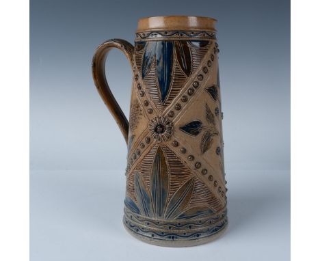 A brown stone colored pitcher decorated with deep blue art of foliage and raised dots arranged in an x shape pattern. Doulton
