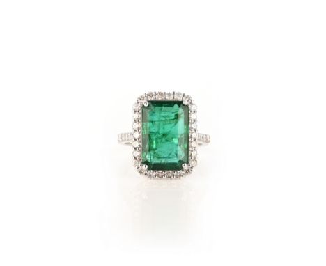 An emerald and diamond ring, claw-set with a step-cut emerald weighing 6.05 carats, within a border of brilliant-cut diamonds