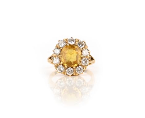 A yellow sapphire and diamond ring, of cluster design, set with a cushion-shaped yellow sapphire within a border of brilliant