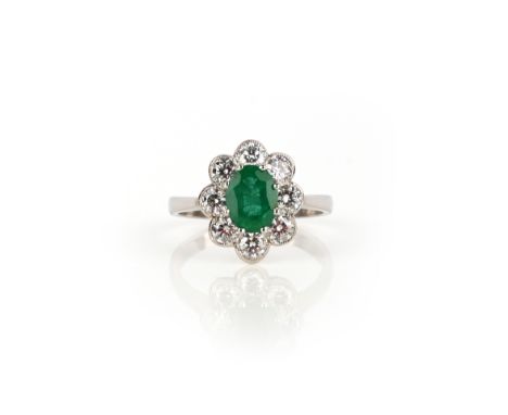 An emerald and diamond cluster ring, the oval-shaped emerald weighs 0.95cts, set within a surround of round brilliant-cut dia