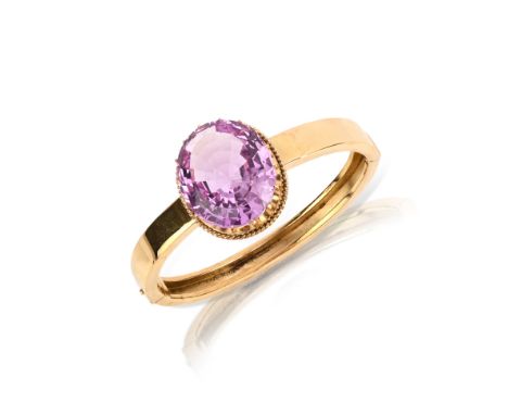 A pink topaz and gold bangle, late 19th century, the hinged bangle set with a large oval pink topaz weighing 34.90 carats, in