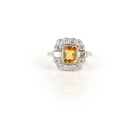 A yellow sapphire and diamond ring, set with a step-cut yellow sapphire, within a border of brilliant-cut and baguette diamon