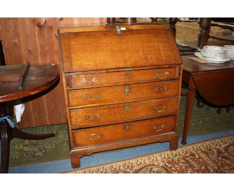 A Georgian Oak Bureau having plain top over the cleated edge fall with ornate brass escutcheon, opening to reveal five pigeon