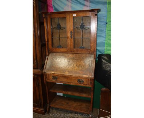 An arts and crafts Oak Bureau Bookcase of small proportion, shaped and moulded top over a pair of opposing ten pane leaded gl
